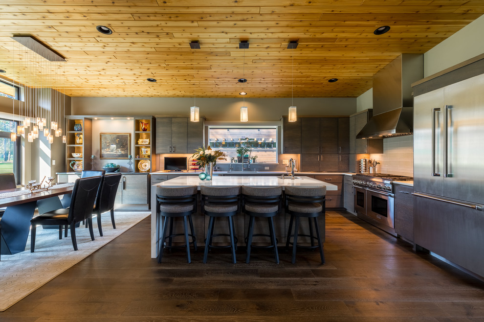 Contemporary l-shaped kitchen/diner in Seattle with flat-panel cabinets, grey splashback, stainless steel appliances, dark hardwood flooring, an island and brown floors.