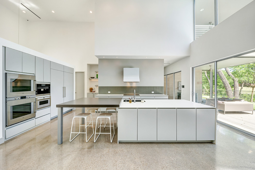 Huge minimalist l-shaped concrete floor and multicolored floor open concept kitchen photo in Dallas with an undermount sink, flat-panel cabinets, white cabinets, solid surface countertops, stainless steel appliances and an island