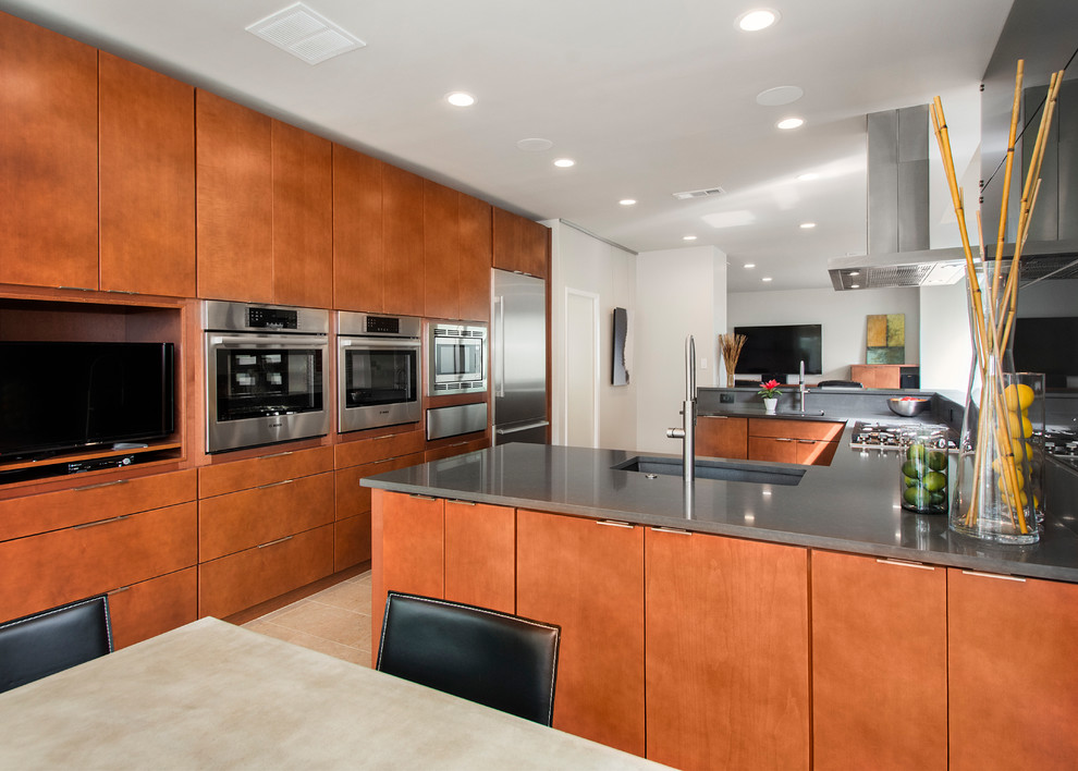 Large modern kitchen in Dallas with beige floors, a submerged sink, flat-panel cabinets, medium wood cabinets, engineered stone countertops, grey splashback, glass tiled splashback, stainless steel appliances and limestone flooring.