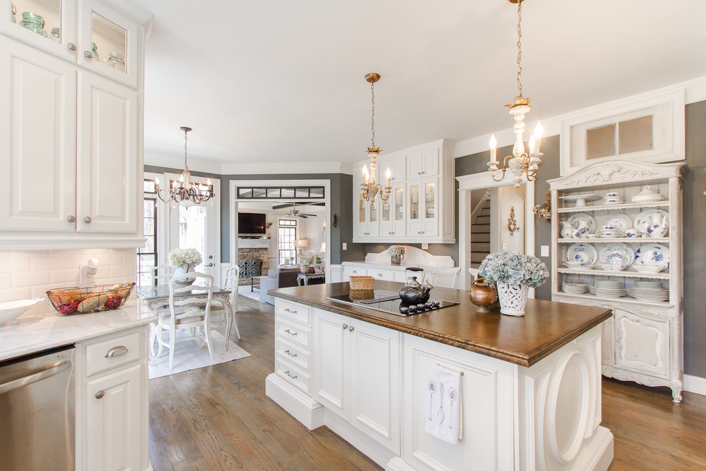 Photo of a traditional kitchen/diner in Atlanta with white cabinets, white splashback, metro tiled splashback, stainless steel appliances, medium hardwood flooring, an island and raised-panel cabinets.