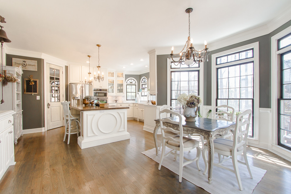 Klassische Wohnküche in L-Form mit profilierten Schrankfronten, weißen Schränken, Küchenrückwand in Weiß, Küchengeräten aus Edelstahl, braunem Holzboden und Kücheninsel in Atlanta