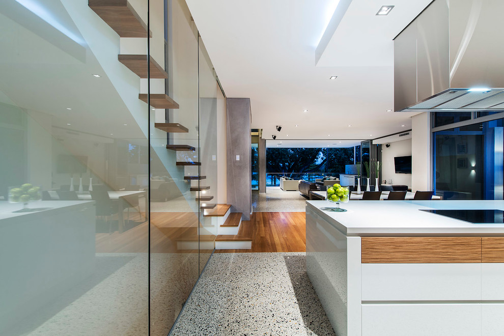 Foto på ett litet funkis kök, med släta luckor, en köksö, en dubbel diskho, vita skåp, bänkskiva i kvarts, vitt stänkskydd, glaspanel som stänkskydd, svarta vitvaror och betonggolv