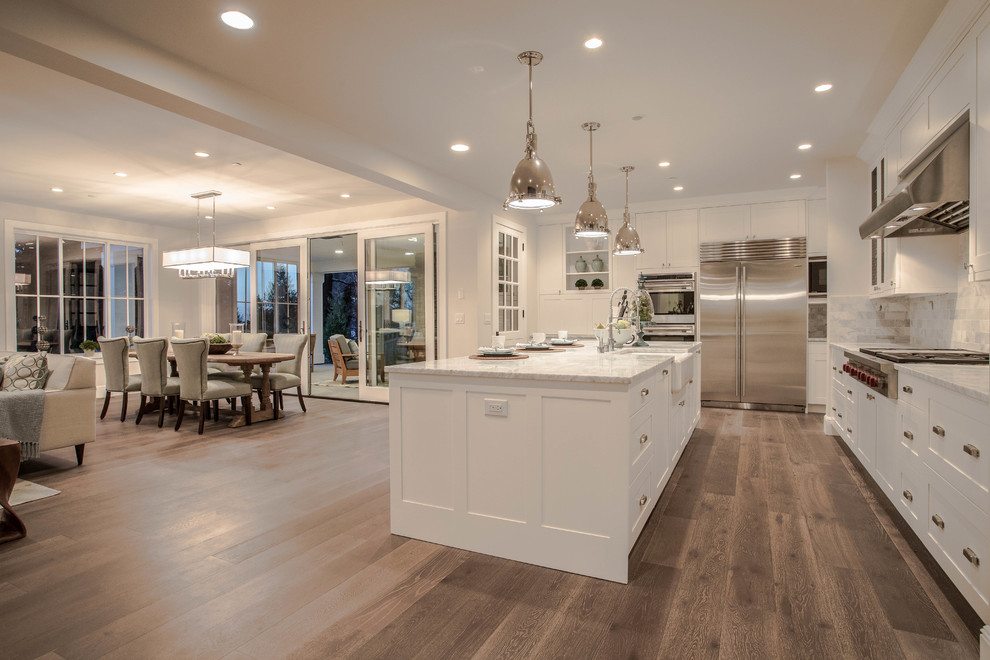 Inspiration for an expansive country l-shaped open plan kitchen in Seattle with a belfast sink, shaker cabinets, white cabinets, marble worktops, white splashback, stone tiled splashback, stainless steel appliances, dark hardwood flooring and an island.