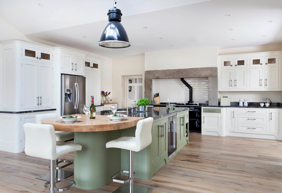 Bild på ett stort lantligt kök, med en undermonterad diskho, skåp i shakerstil, gröna skåp, granitbänkskiva, vitt stänkskydd, stänkskydd i keramik, rostfria vitvaror, ljust trägolv, en köksö och brunt golv