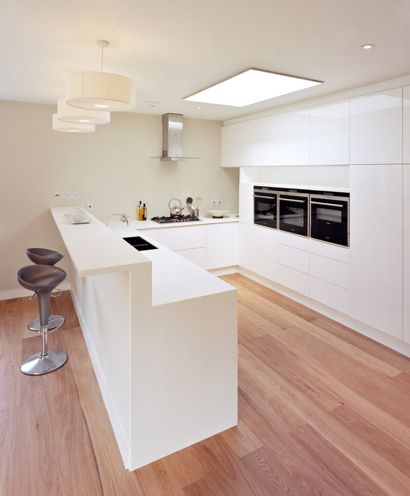 Moderne Küche in U-Form mit Unterbauwaschbecken, flächenbündigen Schrankfronten, weißen Schränken und braunem Holzboden in London
