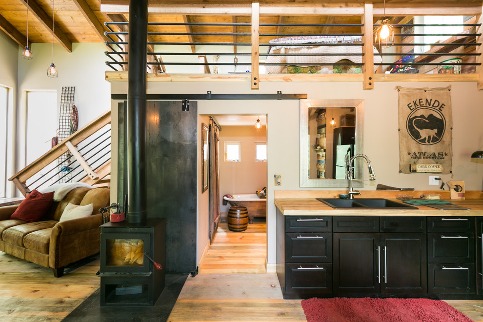 Photo of a small rustic l-shaped kitchen/diner in Denver with a double-bowl sink, shaker cabinets, black cabinets, wood worktops, wood splashback, black appliances, medium hardwood flooring and no island.