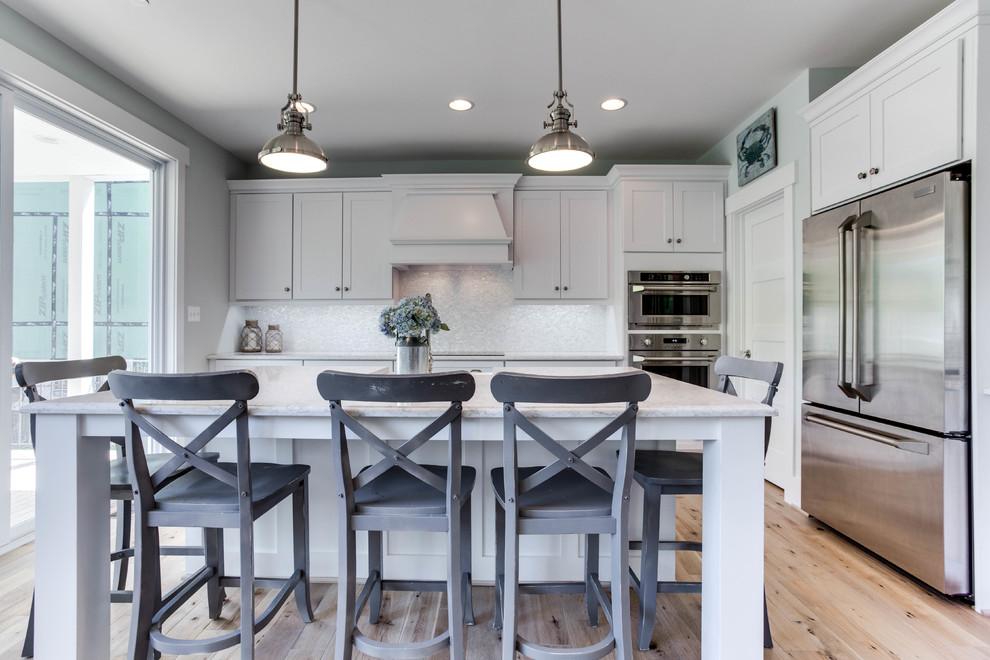 Inspiration for a large coastal light wood floor kitchen remodel in Baltimore with a farmhouse sink, recessed-panel cabinets, white cabinets, quartz countertops, stainless steel appliances and an island