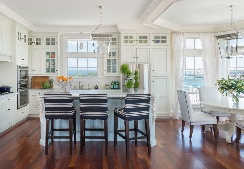 Foto på ett mellanstort maritimt kök och matrum, med luckor med infälld panel, vita skåp, marmorbänkskiva, vitt stänkskydd, stänkskydd i keramik, rostfria vitvaror, mellanmörkt trägolv och en köksö