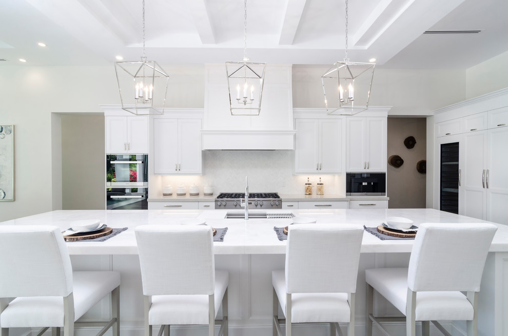 Large beach style kitchen photo in Miami with shaker cabinets, white cabinets, quartzite countertops, white backsplash, an island, an undermount sink and gray countertops