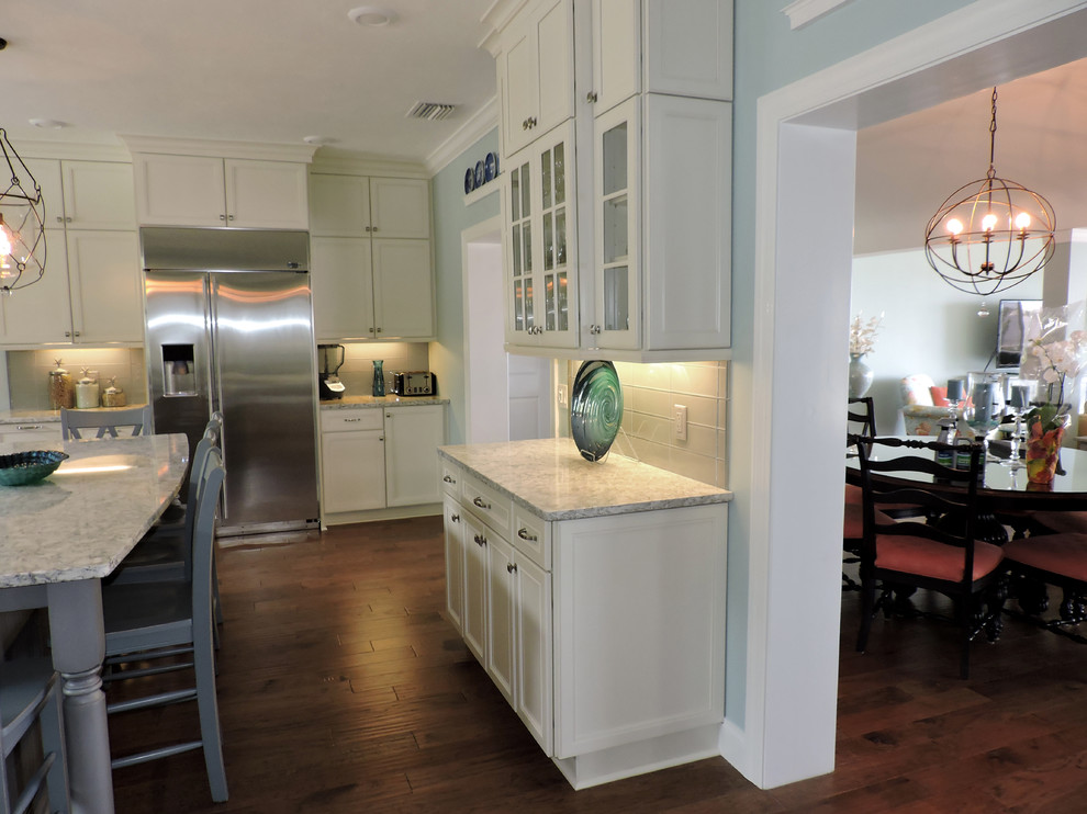 Bild på ett stort funkis kök, med en dubbel diskho, luckor med upphöjd panel, vita skåp, granitbänkskiva, beige stänkskydd, stänkskydd i glaskakel, rostfria vitvaror, mörkt trägolv och flera köksöar