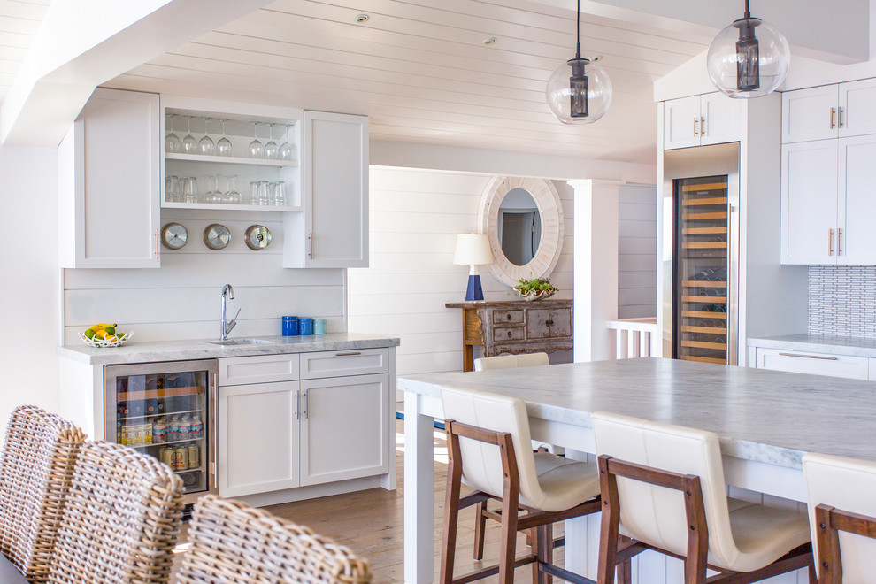 This is an example of a country l-shaped kitchen/diner in Boston with a submerged sink, shaker cabinets, white cabinets, white splashback, light hardwood flooring and an island.