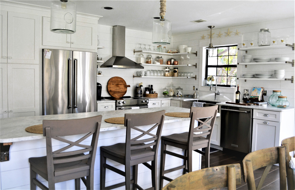 Small beach style l-shaped dark wood floor and brown floor open concept kitchen photo in Charleston with a farmhouse sink, flat-panel cabinets, white cabinets, quartz countertops, white backsplash, wood backsplash, stainless steel appliances and an island