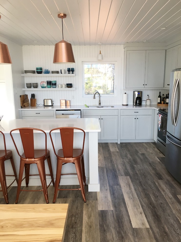 Small beach style l-shaped open plan kitchen in Other with a submerged sink, shaker cabinets, blue cabinets, engineered stone countertops, white splashback, wood splashback, stainless steel appliances, laminate floors, an island and grey floors.