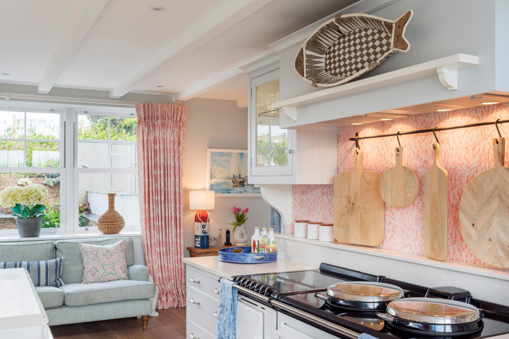 Expansive coastal single-wall kitchen in Devon with beaded cabinets, turquoise cabinets, marble worktops, pink splashback, terracotta splashback, black appliances and white worktops.