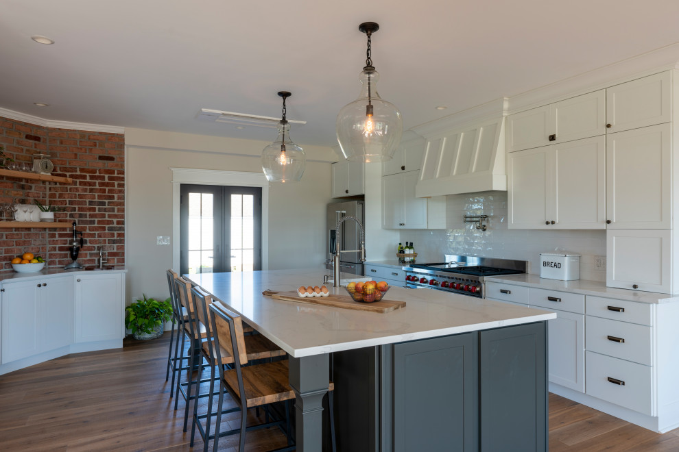 Example of a mid-sized cottage u-shaped light wood floor and beige floor kitchen design in Other with a farmhouse sink, shaker cabinets, white cabinets, quartzite countertops, white backsplash, subway tile backsplash, stainless steel appliances, an island and white countertops