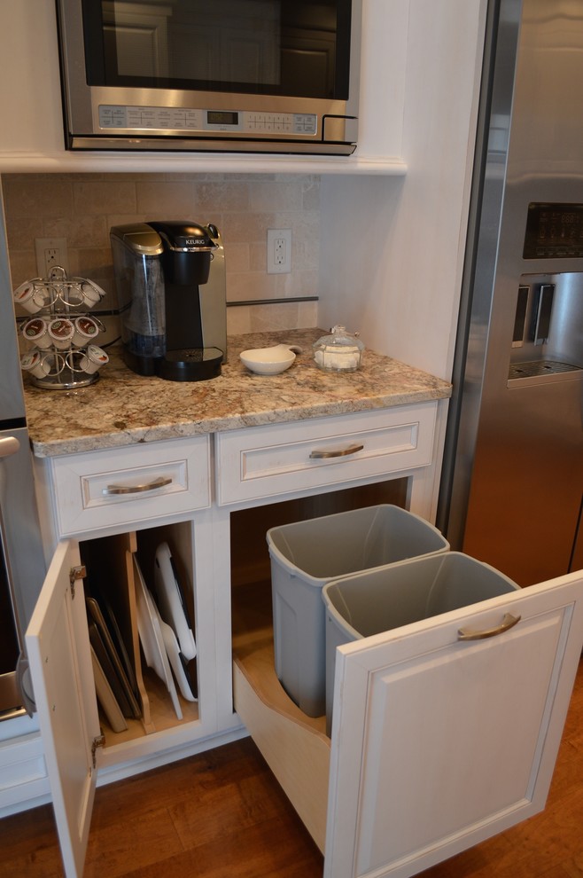 Inspiration for a mid-sized timeless l-shaped medium tone wood floor eat-in kitchen remodel in Cleveland with an undermount sink, raised-panel cabinets, white cabinets, granite countertops, beige backsplash, stone tile backsplash, stainless steel appliances and a peninsula