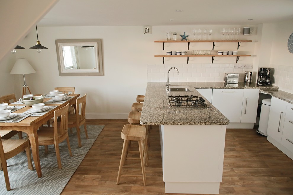 Foto på ett litet maritimt grå kök, med släta luckor, vita skåp, granitbänkskiva, en halv köksö och brunt golv