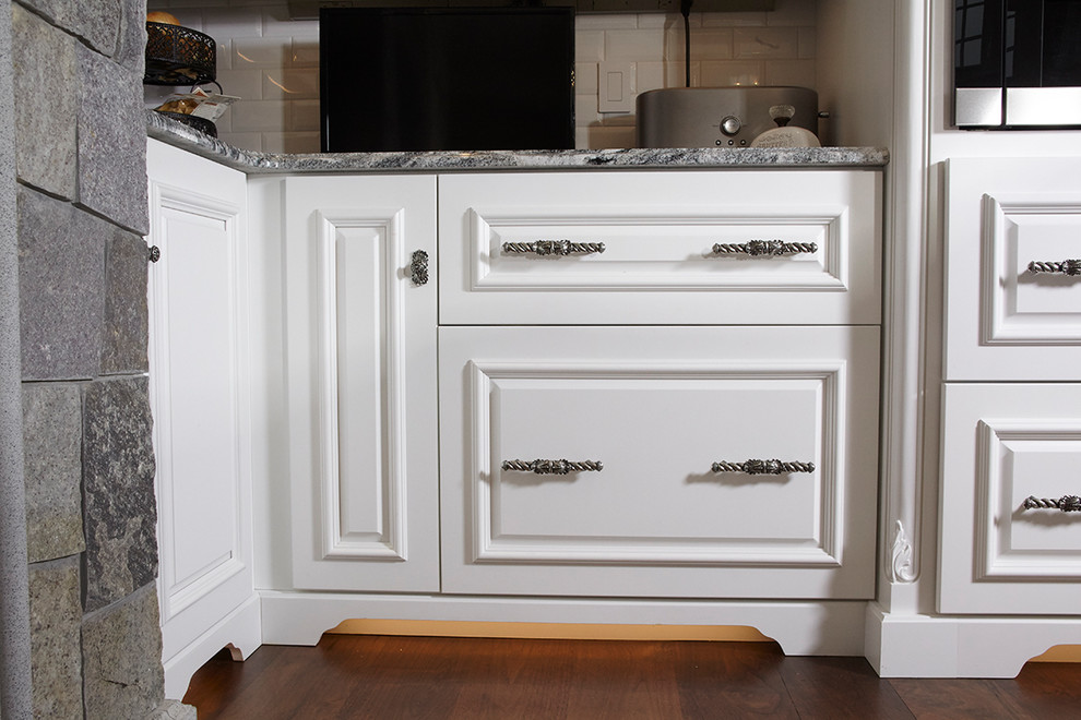 Exempel på ett mycket stort klassiskt kök, med en undermonterad diskho, luckor med upphöjd panel, vita skåp, granitbänkskiva, vitt stänkskydd, stänkskydd i porslinskakel, integrerade vitvaror, mörkt trägolv, en köksö och brunt golv