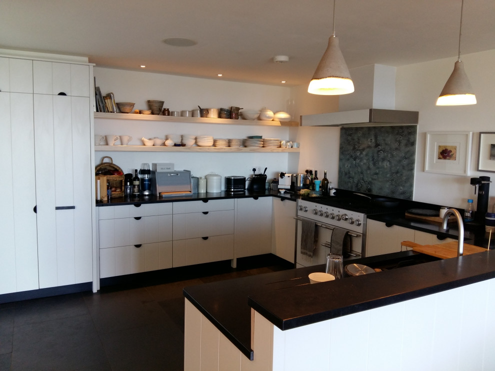 Example of a large beach style u-shaped slate floor and gray floor eat-in kitchen design in Cornwall with a double-bowl sink, flat-panel cabinets, white cabinets, granite countertops, multicolored backsplash and black countertops
