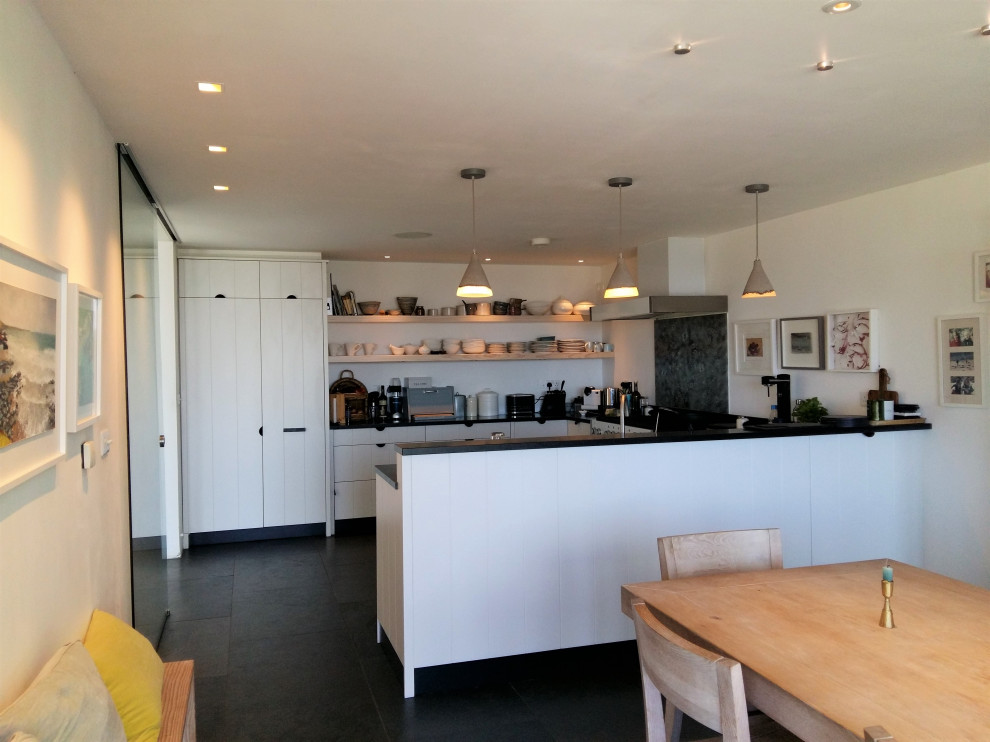 Large coastal u-shaped kitchen/diner in Cornwall with a double-bowl sink, flat-panel cabinets, white cabinets, granite worktops, multi-coloured splashback, slate flooring, grey floors and black worktops.