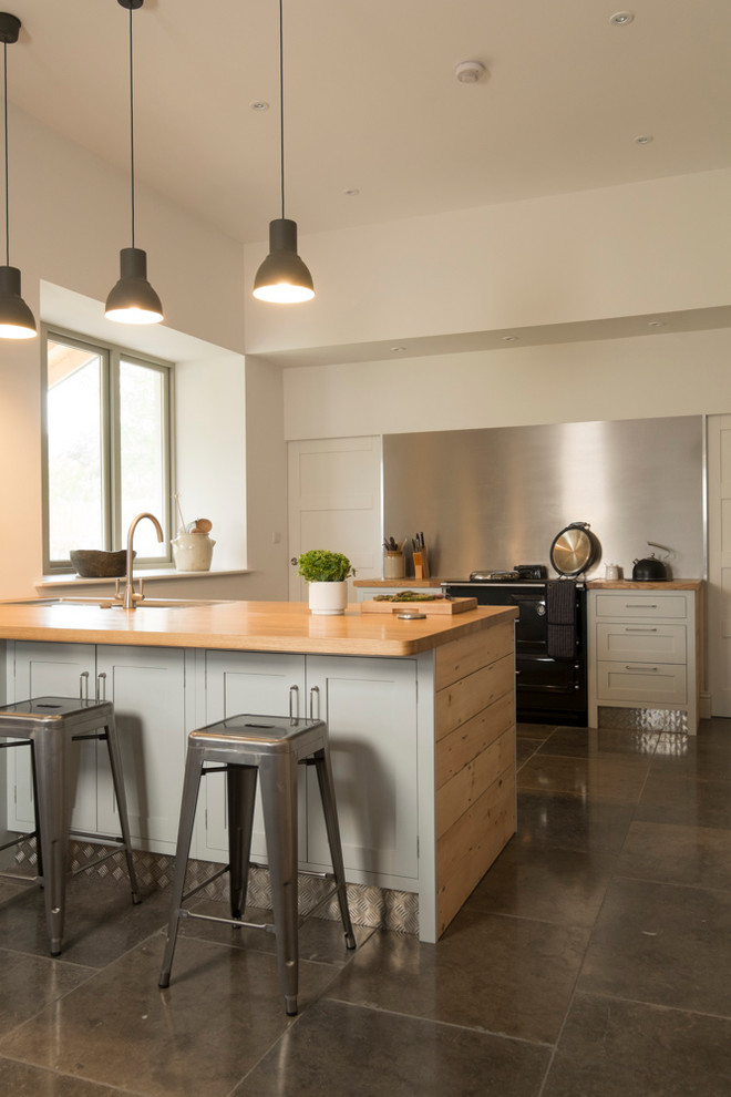 Inspiration for a large contemporary u-shaped kitchen in Cardiff with a double-bowl sink, shaker cabinets, blue cabinets, wood worktops, metallic splashback, black appliances and slate flooring.