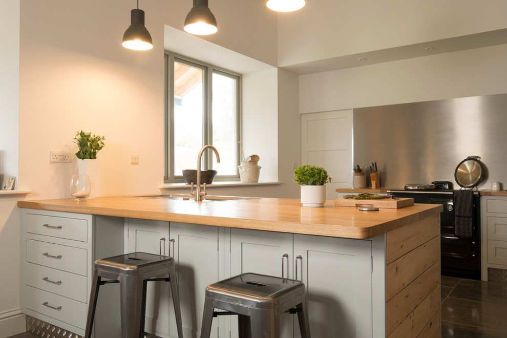 Large contemporary u-shaped kitchen in Cardiff with a double-bowl sink, shaker cabinets, blue cabinets, wood worktops, metallic splashback, black appliances and slate flooring.