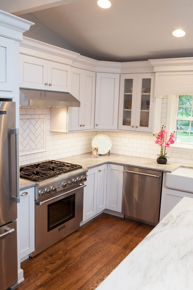 Mid-sized beach style l-shaped medium tone wood floor open concept kitchen photo in Chicago with a farmhouse sink, recessed-panel cabinets, white cabinets, quartz countertops, white backsplash, subway tile backsplash, stainless steel appliances and an island