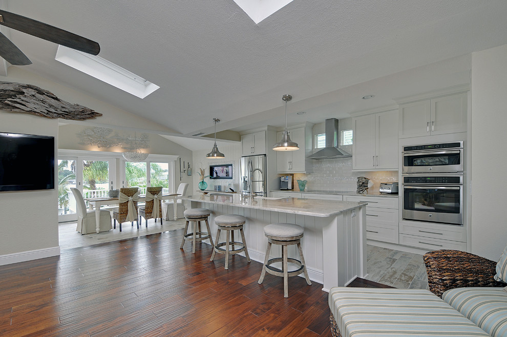 Photo of a medium sized beach style single-wall open plan kitchen in Tampa with a belfast sink, shaker cabinets, white cabinets, granite worktops, white splashback, ceramic splashback, stainless steel appliances, vinyl flooring and an island.