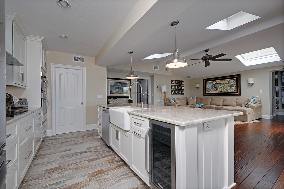 Open concept kitchen - mid-sized coastal single-wall vinyl floor open concept kitchen idea in Tampa with a farmhouse sink, shaker cabinets, white cabinets, granite countertops, white backsplash, ceramic backsplash, stainless steel appliances and an island