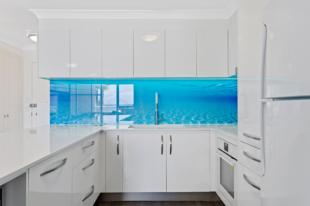 Foto di una piccola cucina stile marinaro con lavello sottopiano, ante lisce, ante bianche, top in quarzo composito, paraspruzzi blu, paraspruzzi con lastra di vetro, elettrodomestici bianchi e top bianco