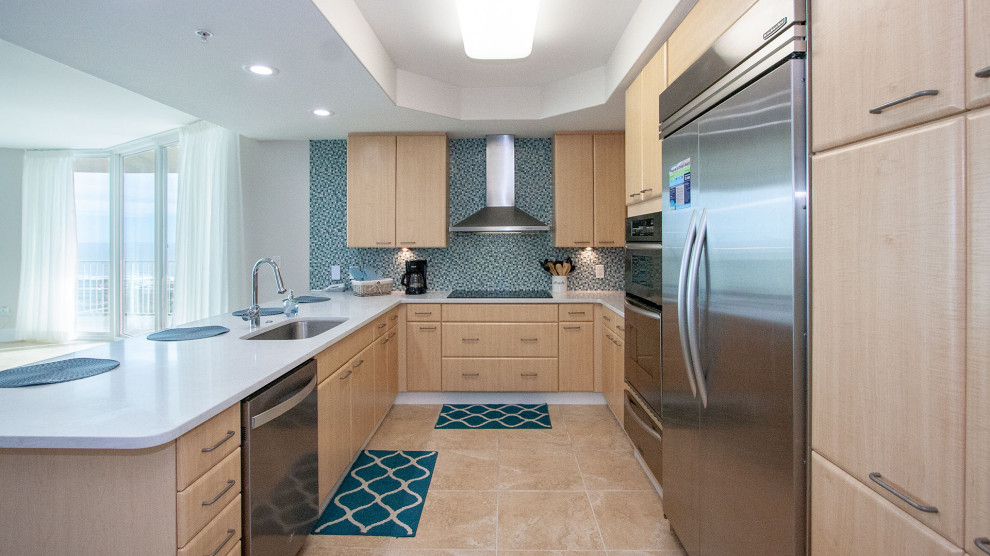 Photo of a medium sized traditional galley kitchen/diner in Austin with a single-bowl sink, flat-panel cabinets, light wood cabinets, engineered stone countertops, blue splashback, glass tiled splashback, stainless steel appliances, porcelain flooring, a breakfast bar, beige floors and white worktops.