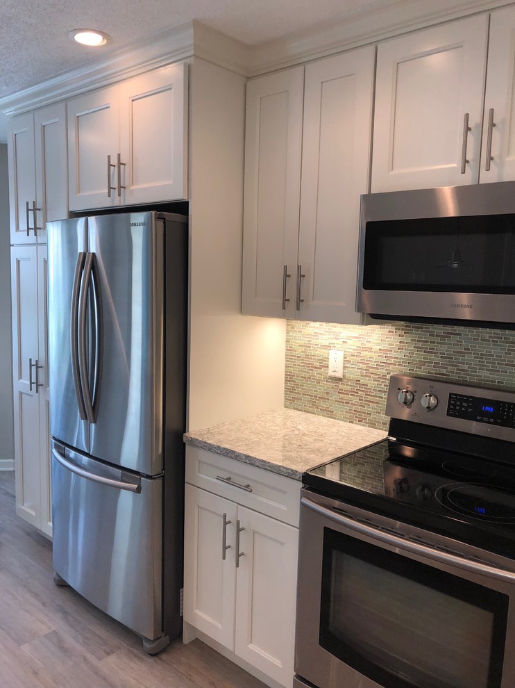 This is an example of a medium sized nautical l-shaped enclosed kitchen in New York with a submerged sink, shaker cabinets, white cabinets, quartz worktops, blue splashback, glass tiled splashback, stainless steel appliances, laminate floors, no island, grey floors and green worktops.