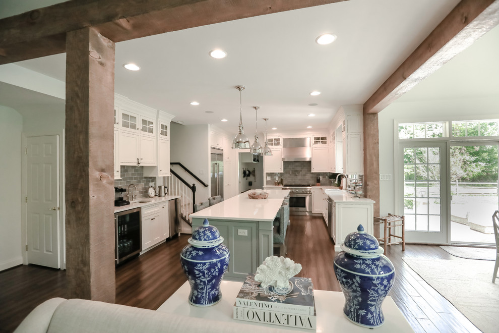 Foto de cocina costera con puertas de armario blancas, electrodomésticos de acero inoxidable, suelo de madera oscura, una isla y suelo marrón