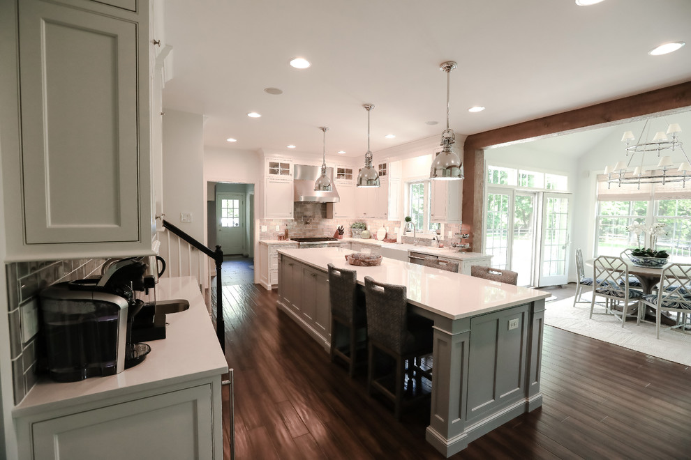 Foto di un cucina con isola centrale costiero con ante bianche, elettrodomestici in acciaio inossidabile, parquet scuro e pavimento marrone