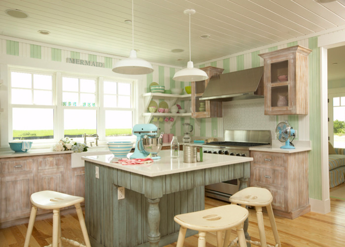 Eat-in kitchen - mid-sized coastal u-shaped light wood floor and brown floor eat-in kitchen idea in Tampa with a farmhouse sink, flat-panel cabinets, beige backsplash, wood backsplash, stainless steel appliances, an island, distressed cabinets and beige countertops