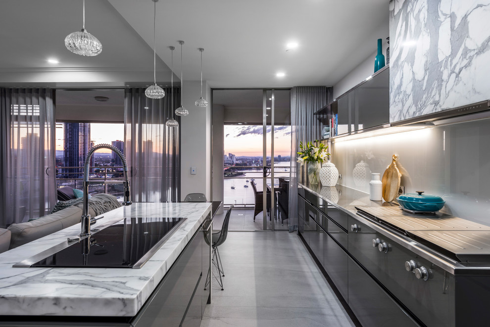 Design ideas for a contemporary galley open plan kitchen in Gold Coast - Tweed with a built-in sink, flat-panel cabinets, grey cabinets, grey splashback, glass sheet splashback, integrated appliances, concrete flooring, an island and grey floors.