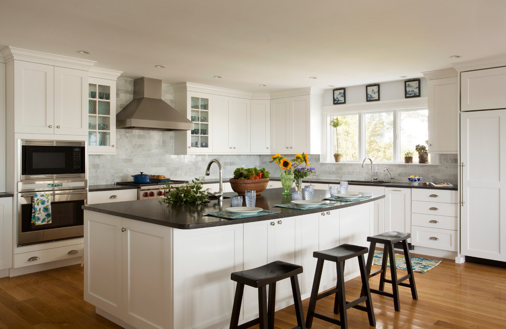 Traditional l-shaped kitchen in Boston with a submerged sink, shaker cabinets, white cabinets, grey splashback, stainless steel appliances, light hardwood flooring and marble splashback.