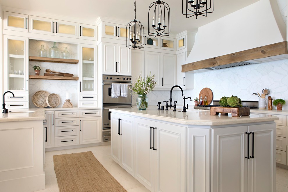 Photo of a nautical u-shaped kitchen in San Diego with raised-panel cabinets, white cabinets, white splashback, stainless steel appliances, an island, beige floors and beige worktops.