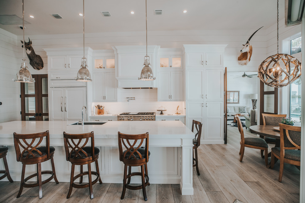 Photo of a rural galley kitchen/diner in Other with a submerged sink, shaker cabinets, white cabinets, white splashback, light hardwood flooring, an island, brown floors and white worktops.