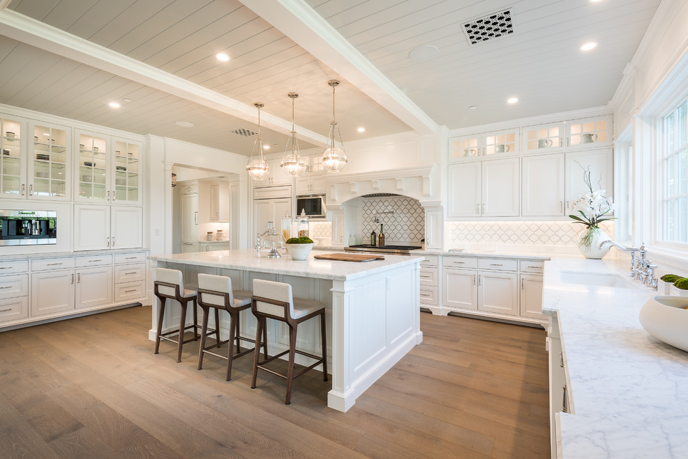 Transitional u-shaped medium tone wood floor and brown floor kitchen photo in Los Angeles with an undermount sink, recessed-panel cabinets, white cabinets, white backsplash, stainless steel appliances, an island and white countertops
