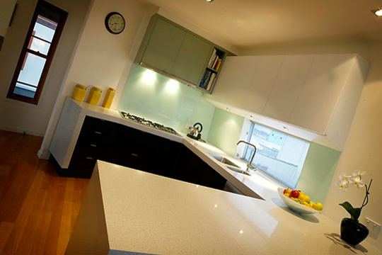 Example of a mid-sized beach style u-shaped medium tone wood floor enclosed kitchen design in Other with a double-bowl sink, granite countertops, green backsplash, glass sheet backsplash, stainless steel appliances and no island
