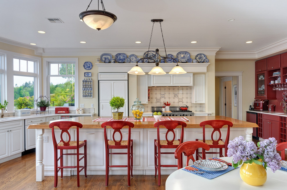Example of a large beach style l-shaped medium tone wood floor eat-in kitchen design in Seattle with wood countertops, paneled appliances, raised-panel cabinets, an island, white cabinets, beige backsplash and ceramic backsplash