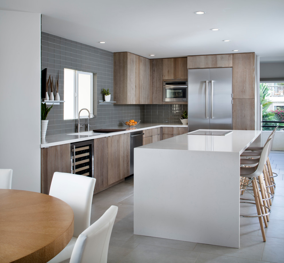 Aménagement d'une cuisine ouverte contemporaine en L et bois brun avec un placard à porte plane, une crédence grise, un électroménager en acier inoxydable, îlot et un sol beige.