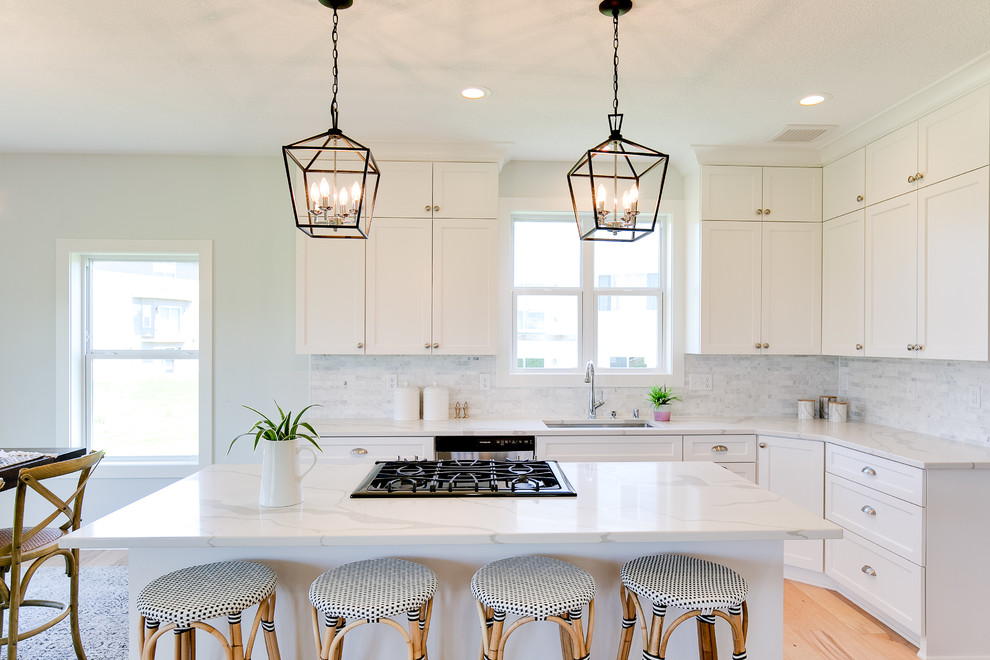 Photo of a medium sized nautical l-shaped kitchen/diner in Minneapolis with a submerged sink, shaker cabinets, white cabinets, grey splashback, marble splashback, stainless steel appliances, light hardwood flooring, an island, beige floors, white worktops and engineered stone countertops.