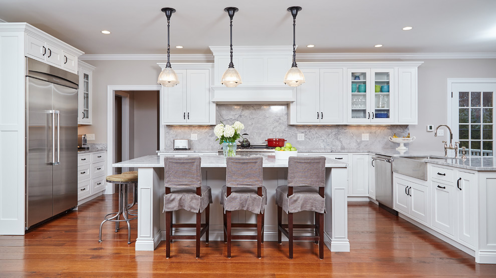 Inspiration for a classic u-shaped kitchen in Boston with a belfast sink, beaded cabinets, white cabinets, marble worktops, white splashback, stainless steel appliances, medium hardwood flooring, an island and stone slab splashback.