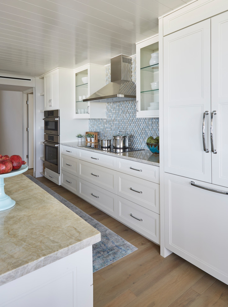Inredning av ett maritimt mellanstort grå grått kök, med en undermonterad diskho, skåp i shakerstil, vita skåp, bänkskiva i kvartsit, flerfärgad stänkskydd, stänkskydd i glaskakel, integrerade vitvaror, mellanmörkt trägolv, en halv köksö och brunt golv