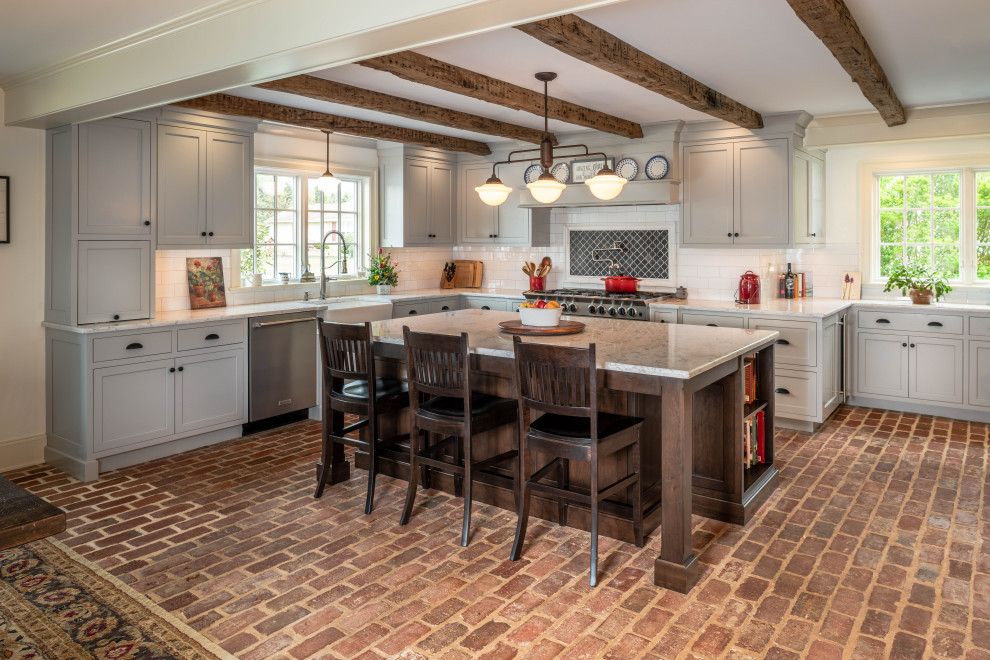 This is an example of a large country kitchen/diner in Philadelphia with white splashback, metro tiled splashback, stainless steel appliances, brick flooring, an island, red floors, exposed beams, flat-panel cabinets, grey cabinets and white worktops.