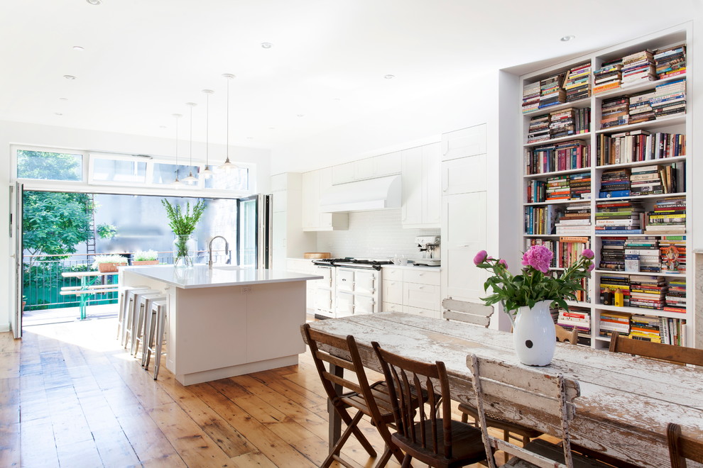 Inspiration for a mid-sized contemporary galley medium tone wood floor and brown floor open concept kitchen remodel in New York with a farmhouse sink, recessed-panel cabinets, white cabinets, quartz countertops, white backsplash, ceramic backsplash, white appliances and an island