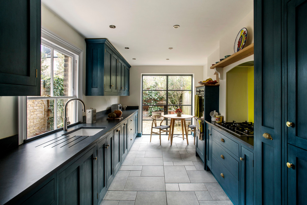 Design ideas for a traditional kitchen in London with a belfast sink, shaker cabinets, blue cabinets, granite worktops, yellow splashback, glass sheet splashback, ceramic flooring and black worktops.
