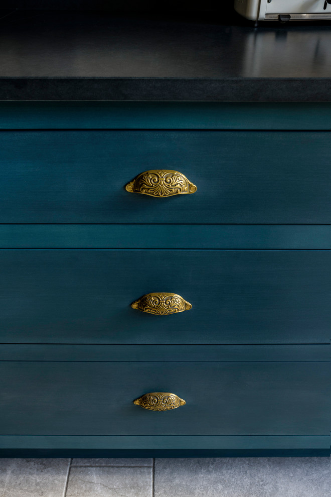 Klassische Küche mit Landhausspüle, Schrankfronten im Shaker-Stil, blauen Schränken, Granit-Arbeitsplatte, Küchenrückwand in Gelb, Glasrückwand, Keramikboden und schwarzer Arbeitsplatte in London